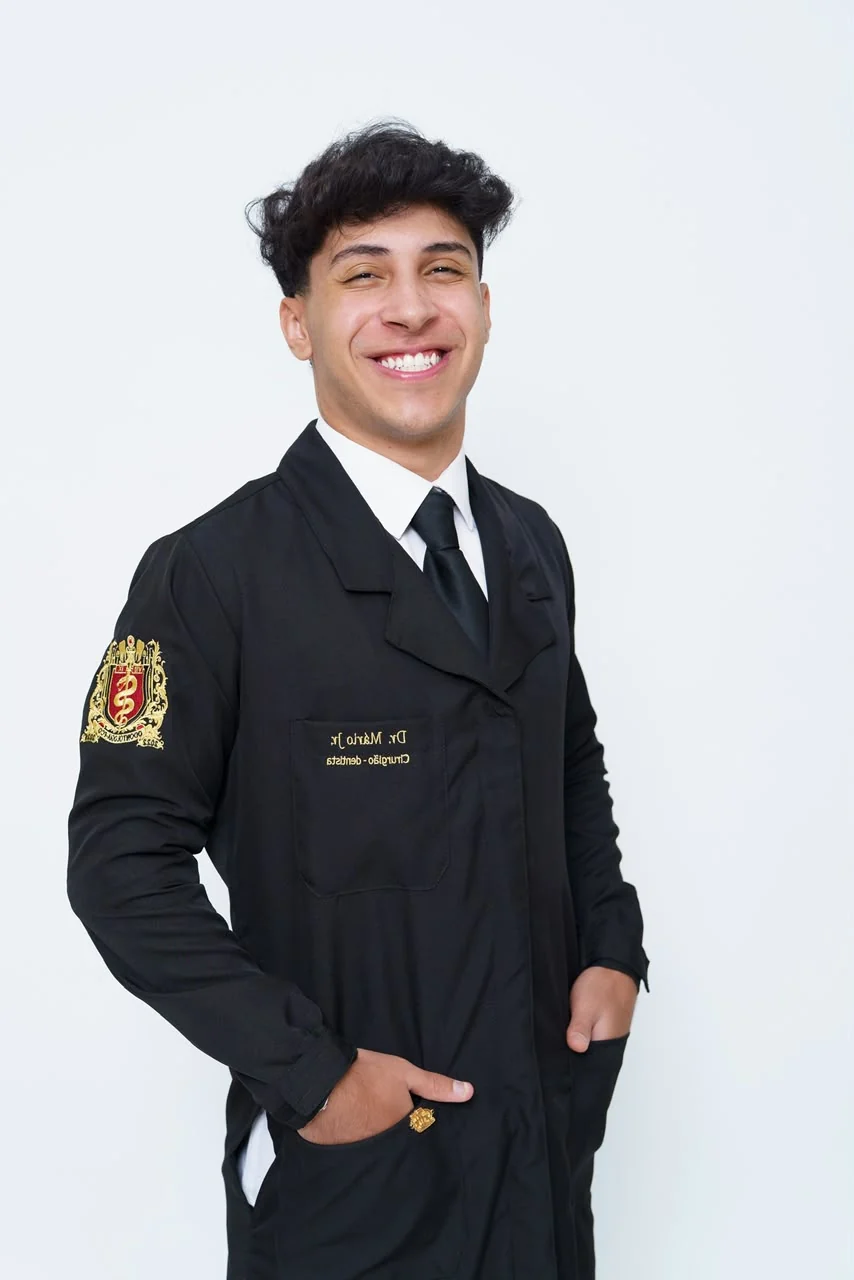 Mário Júnior sorrindo, vestindo jaleco preto com o brasão da turma
